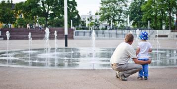 A man and child from the back standing in front of a fountain